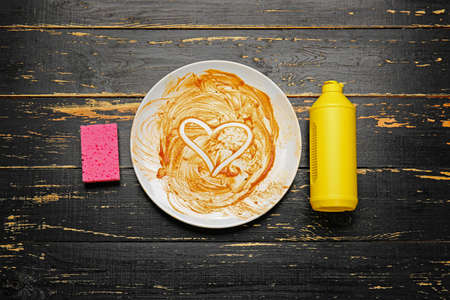 Dirty empty plate, detergent and sponge on dark wooden background