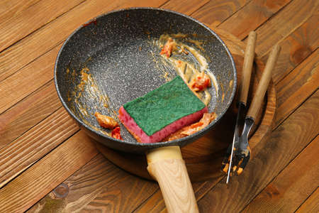Dirty frying pan, sponge and cutlery on wooden backgroundの写真素材
