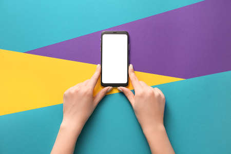 Female hands with mobile phone on color backgroundの写真素材