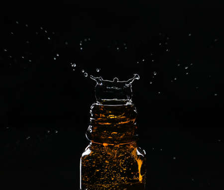 Glass bottle with splashing water on dark backgroundの写真素材