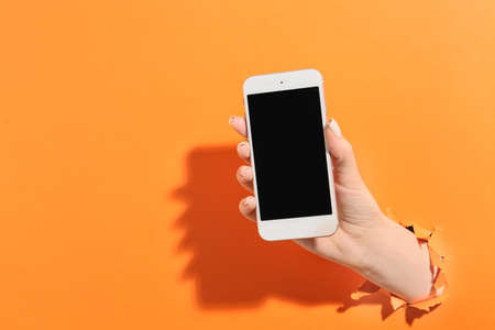 Female hand with mobile phone on color backgroundの写真素材