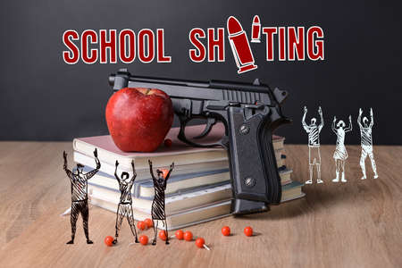 Gun with apple, stack of books and drawn tiny people on table. Problem of shooting at schoolの写真素材