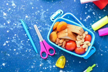 School lunch box with tasty food and stationery on tableの写真素材