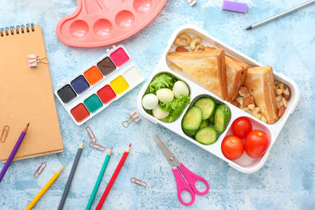 School lunch box with tasty food and stationery on tableの写真素材