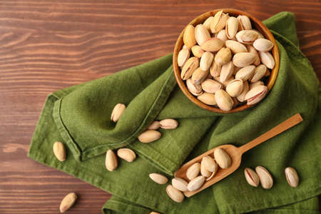 Bowl and scoop with tasty pistachio nuts on wooden background