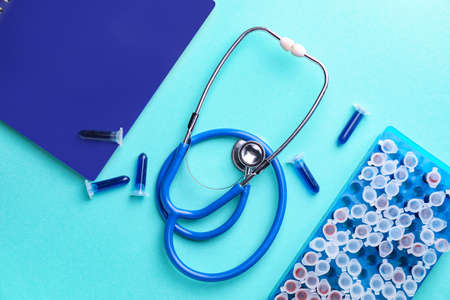 Stethoscope with notebook and test tubes on color background