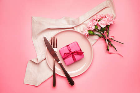 Beautiful table setting with gift and flowers on color backgroundの写真素材
