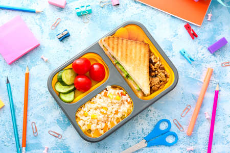 School lunch box with tasty food and stationery on color backgroundの写真素材