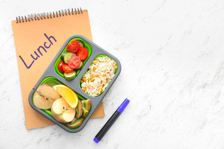 School lunch box with tasty food and notebook on light backgroundの写真素材