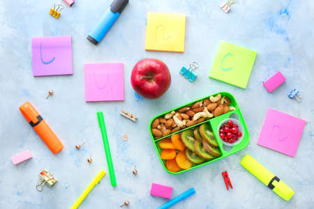 School lunch box with tasty food and stationery on tableの写真素材