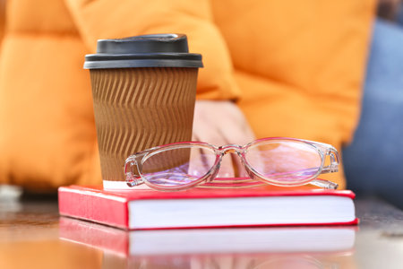 Young woman with book, cup of coffee and eyeglasses sitting on benchの写真素材