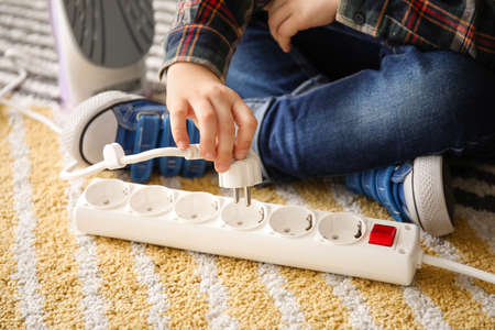 Little boy playing with electric extension cord and iron at homeの写真素材