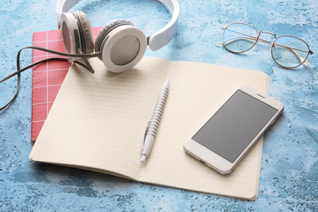 Notebooks with mobile phone, headphones and eyeglasses on color backgroundの写真素材