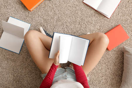 Young woman reading book at home, top view