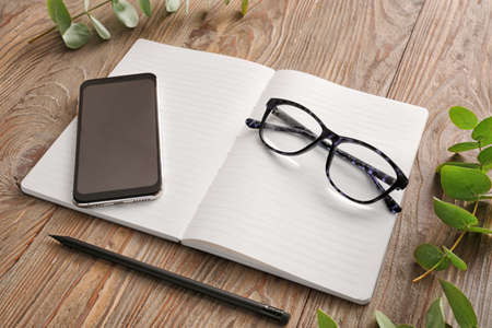 Notebook with mobile phone and eyeglasses on wooden table