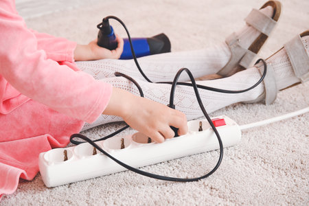Little girl playing with electric extension cord and blow dryer at homeの写真素材