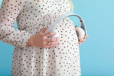 Beautiful pregnant woman putting headphones on her belly against color backgroundの写真素材