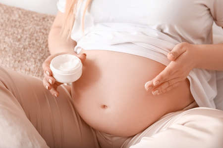 Beautiful pregnant woman applying cream in bedroom, closeupの写真素材
