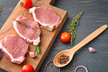 Board with raw pork meat, vegetables and spices on dark wooden backgroundの写真素材