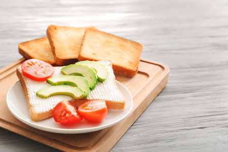 Plate with tasty avocado sandwich and toasted bread on table