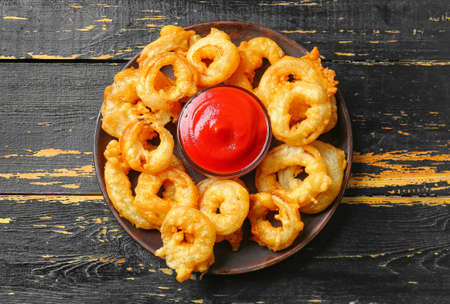 Plate with crispy fried onion rings and sauce on tableの写真素材