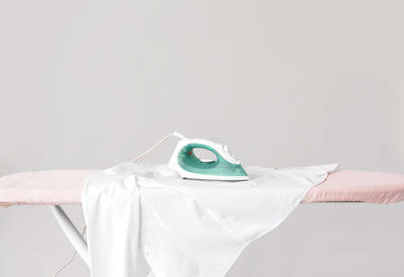 Electric iron with clothes on board against gray backgroundの写真素材