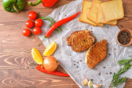 Tasty cooked pork steaks with bread and vegetables on tableの写真素材