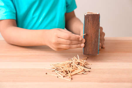 Little African-American boy with matches at table. Child in danger