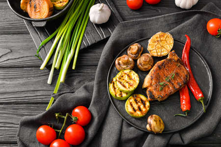 Plate with cooked pork steak and vegetables on tableの写真素材