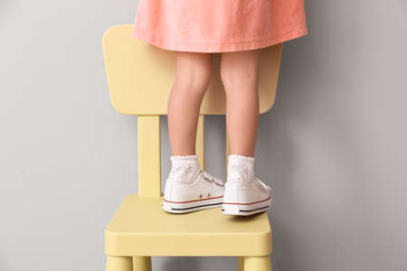 Little African-American girl standing on chair near light wall. Child in dangerの写真素材