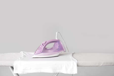 Electric iron with clothes on board against gray backgroundの写真素材