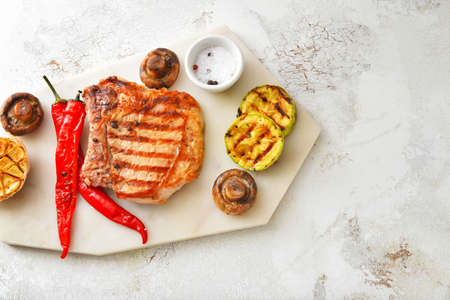 Board with cooked pork steak and vegetables on white backgroundの写真素材