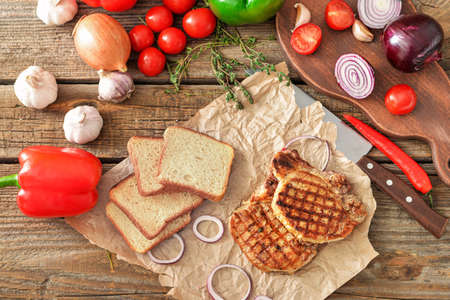 Cooked pork steaks with vegetables and bread on tableの写真素材