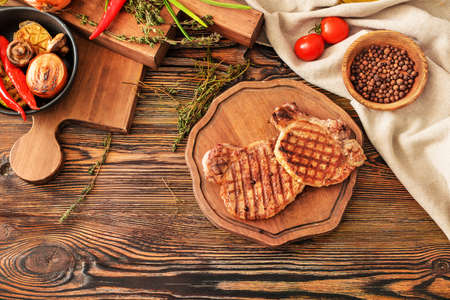 Board with cooked pork steaks, spices and vegetables on tableの写真素材