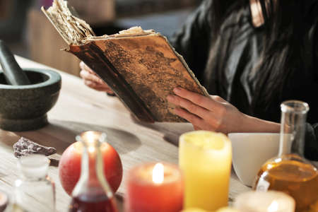 Female alchemist with spell book making elixir in laboratory