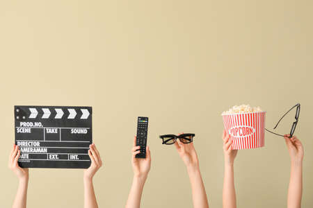 Many hands with popcorn, remote control, movie clapper and eyeglasses on color backgroundの写真素材