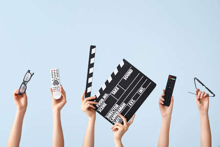 Many hands with remote controls, movie clapper and eyeglasses on color backgroundの写真素材