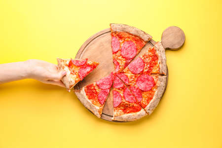 Woman taking slice of tasty pizza from board on color backgroundの写真素材