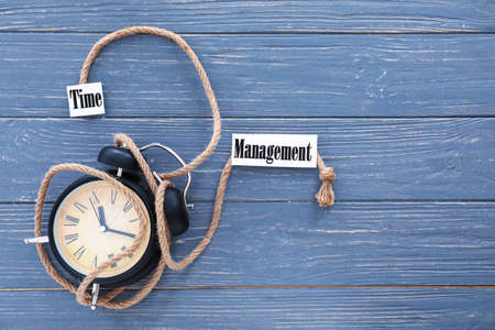 Alarm clock with rope and text TIME MANAGEMENT on wooden backgroundの写真素材