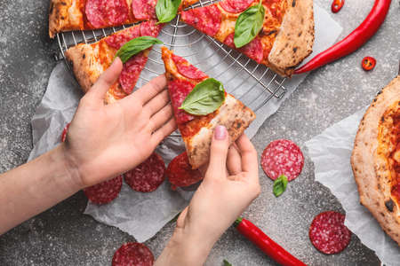 Woman taking slice of tasty pizza on gray backgroundの写真素材