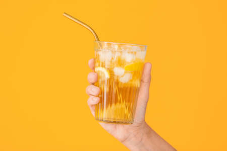 Female hand with cold tea in glass on color backgroundの写真素材