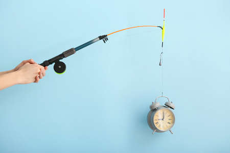 Female hands with fishing rod and alarm clock on color background. Time management conceptの写真素材