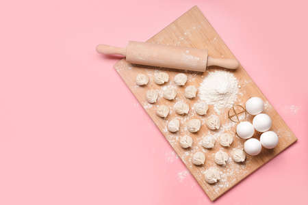 Raw fresh dumplings with rolling pin and eggs on color backgroundの写真素材