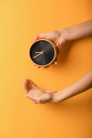 Female hands with clock and sand on color background. Time management conceptの写真素材