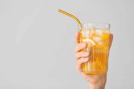 Female hand with cold tea in glass on gray backgroundの写真素材
