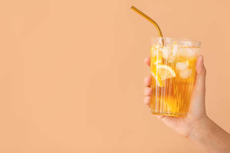 Female hand with cold tea in glass on color backgroundの写真素材