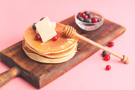 Tasty pancakes with honey, butter and berries on color backgroundの写真素材