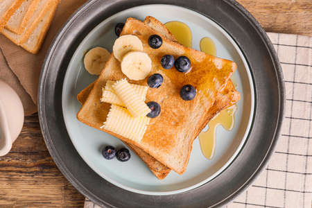 Tasty toasted bread with honey, butter and fruits on plateの写真素材