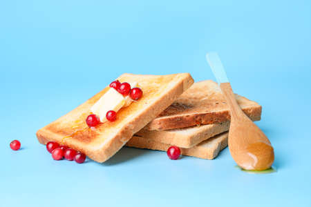 Tasty toasted bread with honey, butter and berries on color backgroundの写真素材
