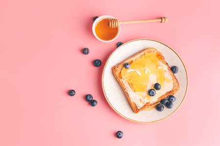 Tasty toasted bread with honey, butter and berries on color backgroundの写真素材